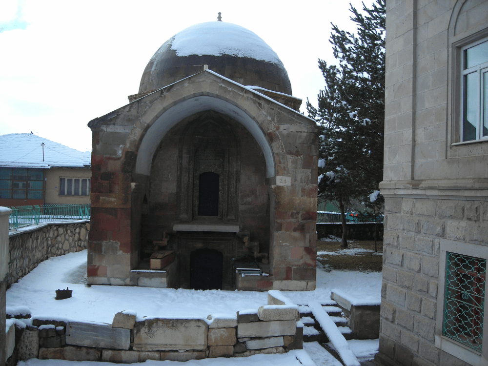 An octagonal Ottoman-era domed mausoleum (kümbet) dated 1587–88, standing in the courtyard of the 'Domed Mosque' in Çayıralan.